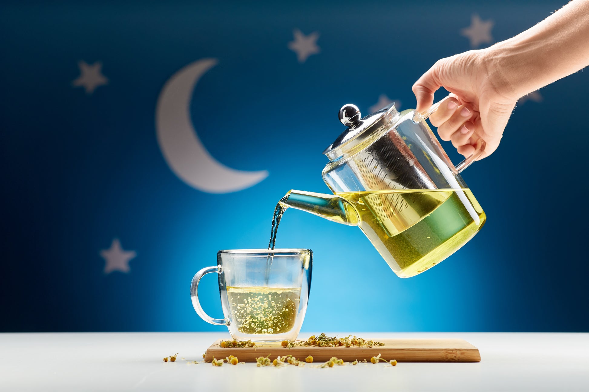 Hand pouring chamomile tea at night with stars and moon background